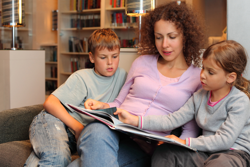 Mom reading with young son and daughter on the couch. Little girl is turning the page together with her mom.